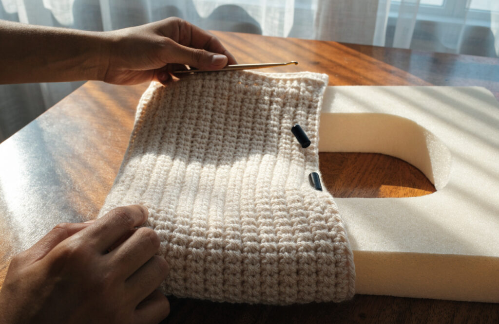Hands crocheting a rectangular dog bed cover in single crochet next to the foam insert