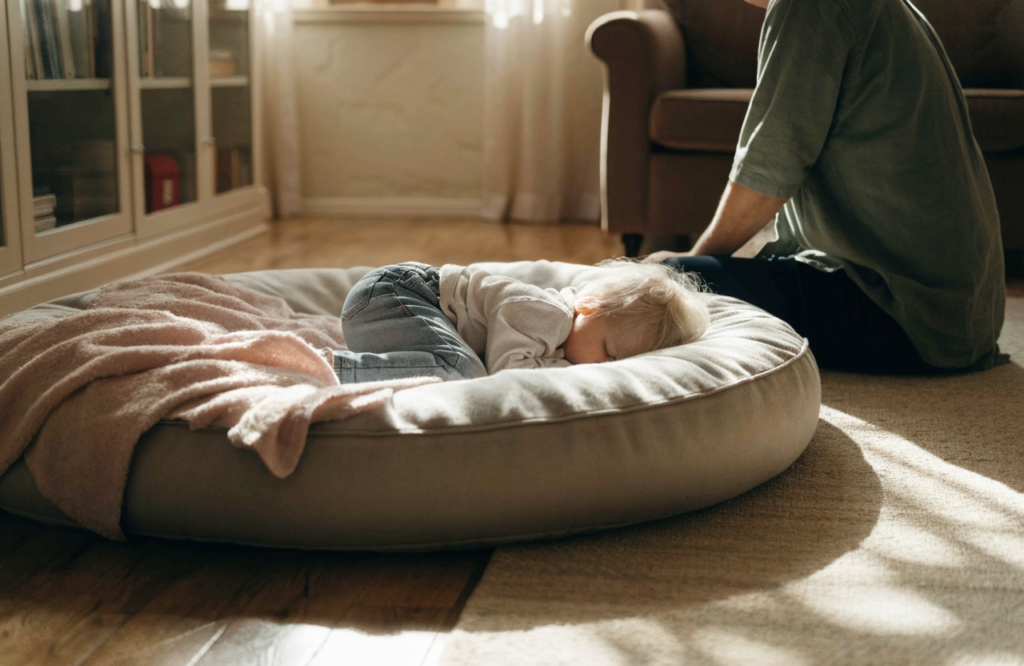 Toddler napping on a large floor dog bed with a parent beside